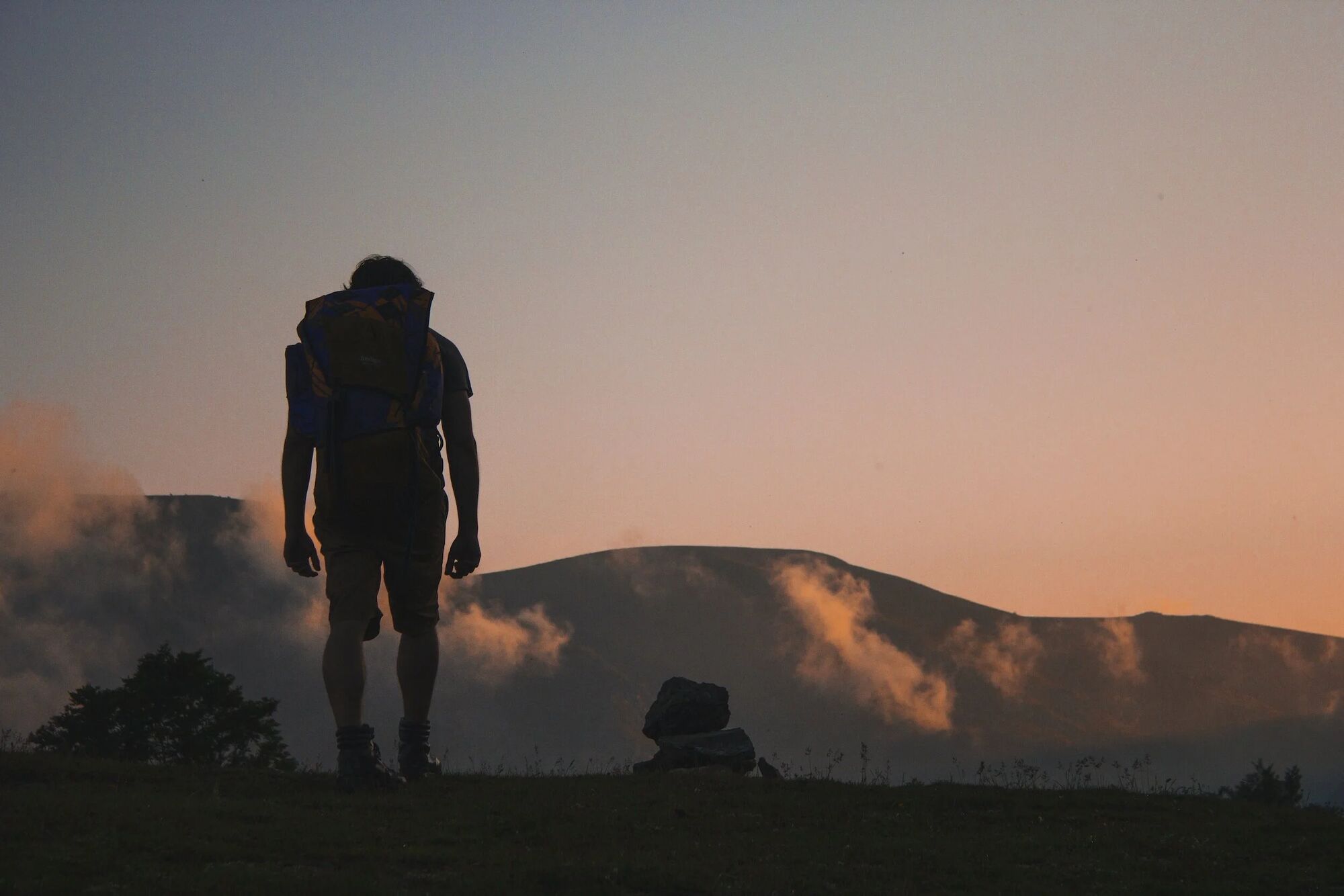 Hiker pausing at sunrise on a Colorado ridgeline, backpack on, mountains glowing in alpenglow